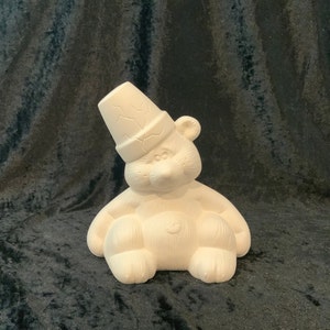 May include: White ceramic bear figurine wearing a hat. The bear is sitting with its legs crossed and has a small heart on its chest.