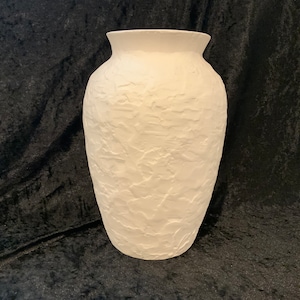 May include: White ceramic vase with a textured surface. The vase has a rounded body and a wide opening.