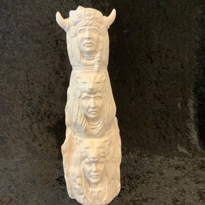 May include: White ceramic totem pole with three carved faces. The top face has horns and feathers. The middle face has a wolf or dog head. The bottom face has a wolf or dog head.