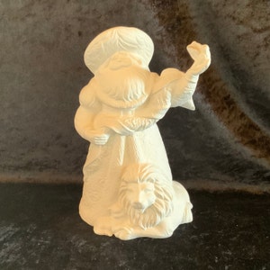 May include: White ceramic figurine of Santa Claus with a lion at his feet. Santa is wearing a hat and a long robe with a decorative pattern. He is holding a scroll in his left hand and a staff in his right hand.