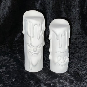 May include: Two white ceramic candle holders shaped like melting candles with faces. The candle holder on the left has a grumpy face and the candle holder on the right has a happy face.
