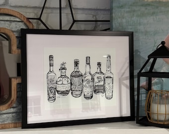 May include: Black and white line art print of seven different bottles of liquor in a black frame. The bottles are arranged in a row and labeled with the names of the brands. The print is on a white background.