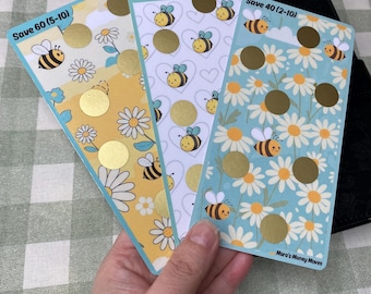 May include: Three floral-themed scratch-off cards with bee and daisy designs. Each card has gold scratch-off circles and text indicating savings amounts. The cards are yellow, white, and blue, with the text "Save 60 (5-10)", "Save 50 (3-10)", and "Save 40 (2-10)".