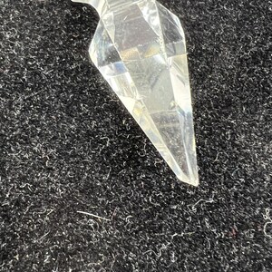 Puede incluir: Un objeto de cristal transparente y facetado con un extremo puntiagudo. El cristal tiene un dise&ntilde;o geom&eacute;trico y refleja la luz, creando un efecto brillante. El objeto est&aacute; sobre un fondo oscuro y texturizado.