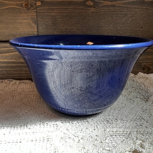 May include: A large, deep blue ceramic bowl with a wide rim. The bowl is sitting on a white crocheted doily.