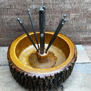 May include: A wooden nutcracker set with a natural bark edge. The set includes a central nutcracker and four metal picks. The wooden bowl has a light brown interior and a darker, textured exterior.