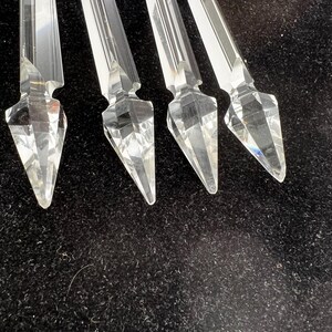 Puede incluir: Cuatro piezas decorativas de cristal transparente y facetado con un extremo puntiagudo y una parte superior rectangular. Los cristales est&aacute;n dispuestos sobre una superficie oscura y texturizada, mostrando sus cualidades reflectantes y dise&ntilde;o geom&eacute;trico.