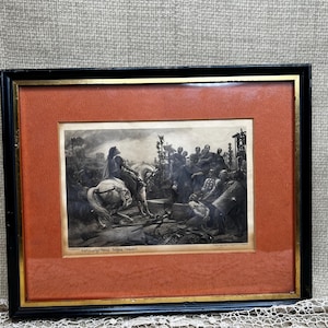 May include: Framed black and white print depicting a historical scene with figures on horseback and a crowd. The print is set within a gold-toned border and a rust-colored mat, encased in a black frame. The print has text at the bottom.