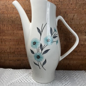 May include: White ceramic coffee pot with a blue and gray floral design. The pot has a rounded body and a spout on one side. The lid is white and has a knob on top.
