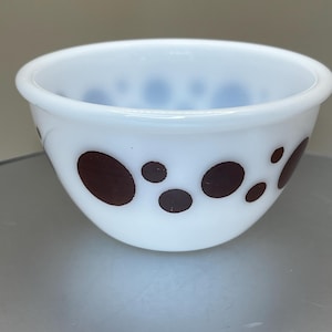 May include: White glass bowl with brown polka dots. The bowl has a rounded shape and a smooth, glossy finish. The brown dots vary in size and are evenly spaced around the exterior of the bowl. A classic kitchenware item.