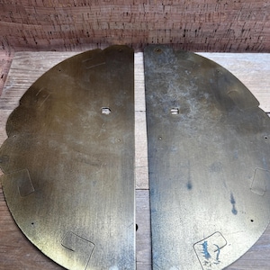 May include: Two antique brass-colored metal door panels. Each panel is semi-circular with decorative scalloped edges and cut-out geometric shapes. The panels have a vintage, aged appearance with slight discoloration.