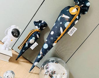 Può includere: Due coni di tessuto blu e nero con una stampa a tema spaziale. I coni hanno un cordoncino giallo e un'etichetta con i nomi "Julian" e "Mio".