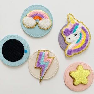 Könnte beinhalten: Fünf bunte Filzpatches auf weißem Hintergrund. Die Patches sind rund und zeigen einen Regenbogen, ein Einhorn, einen Blitz, einen Stern und einen schwarzen Kreis.