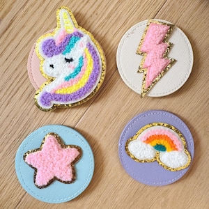Könnte beinhalten: Vier runde Filzpatches mit verschiedenen Designs. Ein pinkfarbenes Einhorn mit einer Regenbogenmähne, ein pinkfarbener Blitz, ein pinkfarbener Stern und ein Regenbogen mit Wolken.