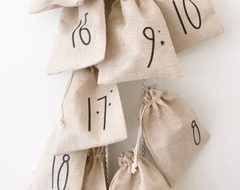 May include: A beige burlap advent calendar with numbers 5 through 18 printed on each of the small pouches. The pouches are hanging in a descending order from a string.