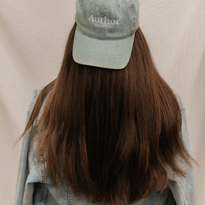 Könnte beinhalten: Eine Person trägt eine hellblaue Jeansjacke und eine hellblaue Baseballkappe mit dem Wort "Autor" in weiß aufgestickt auf der Vorderseite.