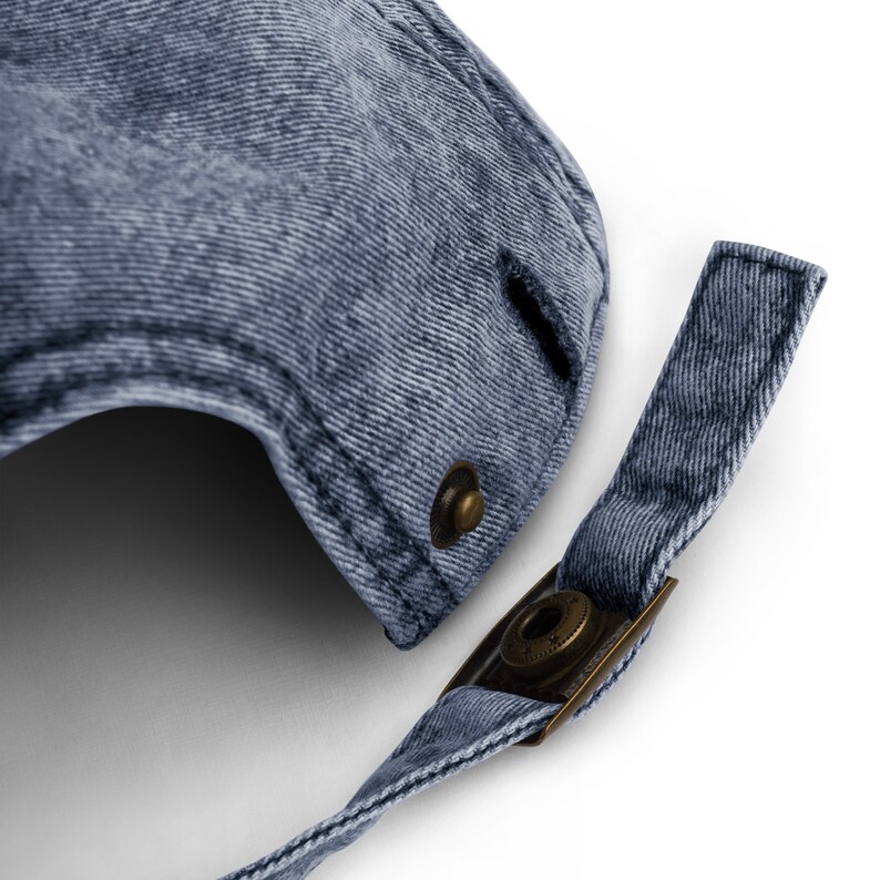 Puede incluir: Una gorra de b&eacute;isbol de mezclilla azul con una correa y una hebilla de metal. La gorra tiene un aspecto desgastado y un peque&ntilde;o agujero cerca de la parte superior.