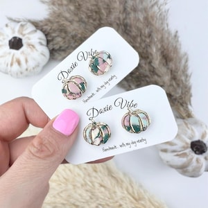 Pu&ograve; includere: Due paia di orecchini a forma di zucca. Gli orecchini sono rosa, verdi e dorati. Sono su biglietti bianchi con il testo "Doxie Vibe" e "Handmade... with my dog nearby".
