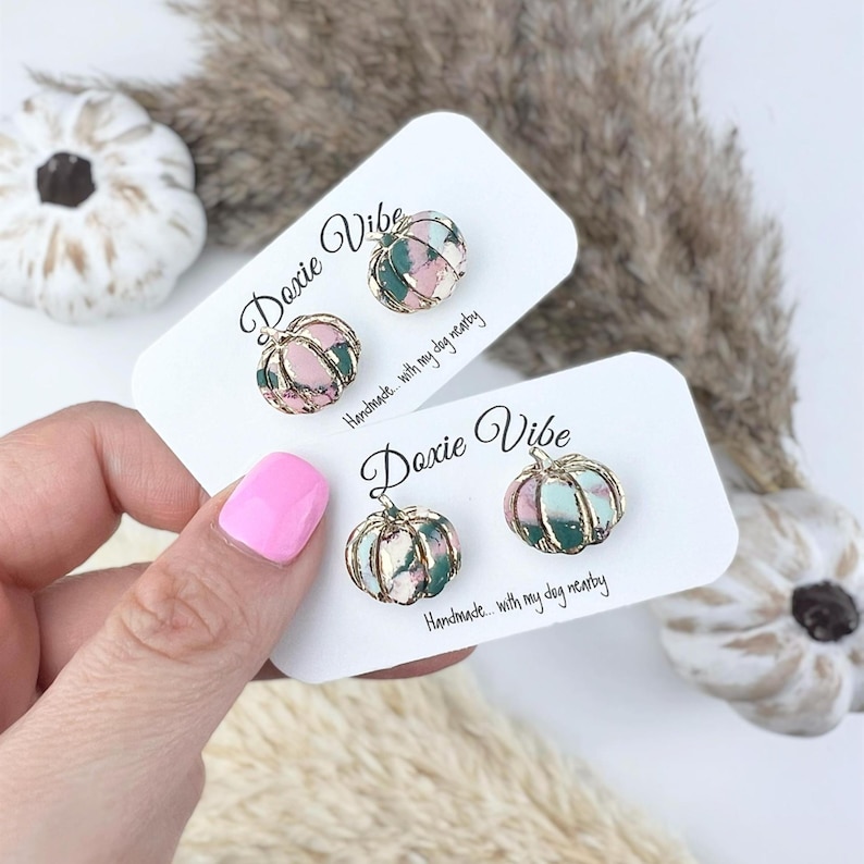 Pu&ograve; includere: Due paia di orecchini a forma di zucca. Gli orecchini sono rosa, verdi e dorati. Sono su biglietti bianchi con il testo "Doxie Vibe" e "Handmade... with my dog nearby".