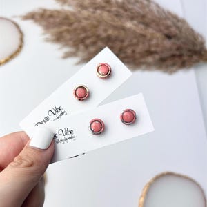 Peut inclure: Quatre paires de boucles d'oreilles clous roses avec des accents dor&eacute;s et argent&eacute;s sont pr&eacute;sent&eacute;es sur des cartons blancs. Les cartes portent l'inscription "Dixie Vibe with my dynasty". Les boucles d'oreilles sont rondes avec un centre en relief et une bordure m&eacute;tallique.
