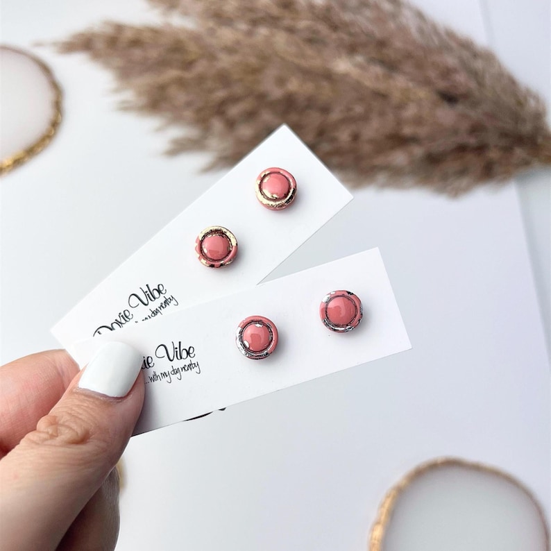 Peut inclure: Quatre paires de boucles d'oreilles clous roses avec des accents dor&eacute;s et argent&eacute;s sont pr&eacute;sent&eacute;es sur des cartons blancs. Les cartes portent l'inscription "Dixie Vibe with my dynasty". Les boucles d'oreilles sont rondes avec un centre en relief et une bordure m&eacute;tallique.