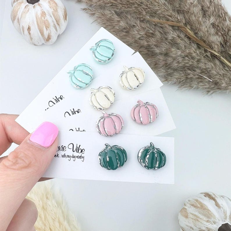 Pu&ograve; includere: Orecchini a forma di zucca in tonalit&agrave; pastello, tra cui azzurro, bianco, rosa e verde, con dettagli argentati. Gli orecchini sono presentati su biglietti bianchi con il testo "...Xie Vibe".
