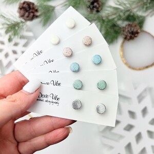 May include: Six pairs of small, round, glitter stud earrings on white cards. The cards have the text "Dovie Vibe" and "Enchant with my dainty" on them. The earrings are in the colors white, pink, light blue, green, and silver.
