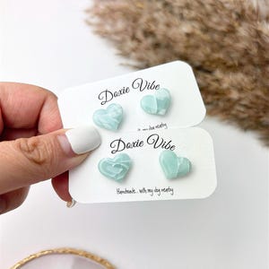 May include: Two cards with the text "Doxie Vibe" and a heart-shaped design. The hearts are made of a light blue and white marbled material. The text on the cards reads "Handmade... with my dog nearby".