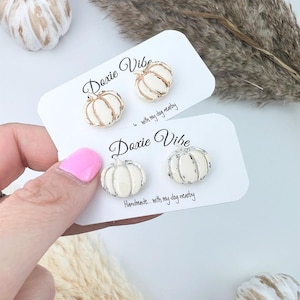 Pu&ograve; includere: Due paia di orecchini a forma di zucca su biglietti bianchi. Un paio ha dettagli in metallo dorato, l'altro argentato. I biglietti riportano "Doxie Vibe" e "Handmade... with my dog nearby."