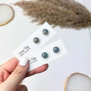 Peut inclure: Deux paires de boucles d'oreilles &agrave; clous avec un centre en pierre grise et une bordure m&eacute;tallique dor&eacute;e ou argent&eacute;e. Les boucles d'oreilles sont pr&eacute;sent&eacute;es sur des cartes blanches avec le texte "Dovie Vibe Handmade with my day today".