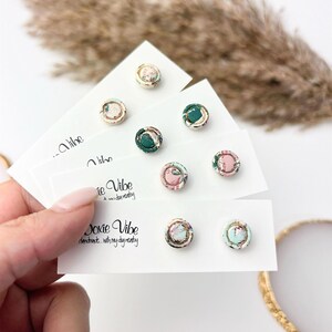 May include: A collection of handmade stud earrings with floral fabric designs. The earrings are displayed on white cards, with the text "Doxie Vibe" and "handmade... with my dog nearby". The earrings feature gold-colored metal accents.