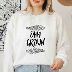May include: White sweatshirt with black text that reads "OHM GROWN" and a graphic of two bundles of sage.