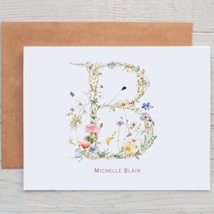 May include: A white card with a floral letter B made of watercolor flowers in shades of pink, blue, yellow, and green. The name "Michelle Blair" is printed in pink below the letter.