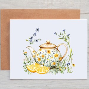 May include: Greeting card featuring a watercolor illustration of a teapot adorned with yellow flowers and a matching lid. Two lemon slices are in the foreground. The card is set against a light blue background, with a brown envelope behind it.