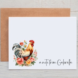 May include: A white card with a rooster illustration and floral accents. The rooster is brown, red, and yellow with a blue tail. The flowers are pink, yellow, and orange. The text "a note from Gabriella" is printed at the bottom of the card.