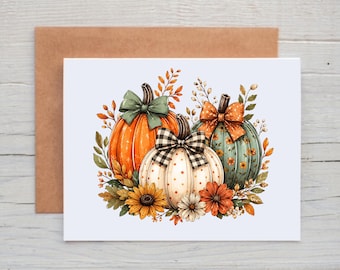 May include: A greeting card featuring an illustration of three pumpkins decorated with bows. One orange pumpkin has a green bow, a white pumpkin has a black and white checkered bow, and a teal pumpkin has an orange polka dot bow, surrounded by flowers.