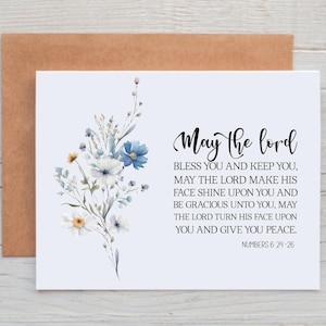 May include: A white greeting card with the text "May the lord" and a floral watercolor design in blue, white, and yellow. The card includes a Bible verse from Numbers 6:24-26 and is paired with a brown envelope.