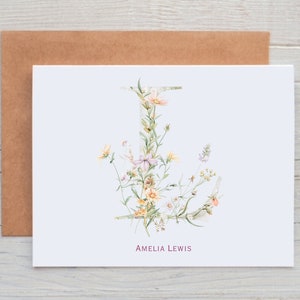 Pu&ograve; includere: Un biglietto bianco con un'illustrazione ad acquerello di una lettera J floreale. La lettera &egrave; composta da diversi fiori e foglie in tonalit&agrave; di rosa, giallo e verde. Il testo "Amelia Lewis" &egrave; stampato in rosa nella parte inferiore del biglietto.