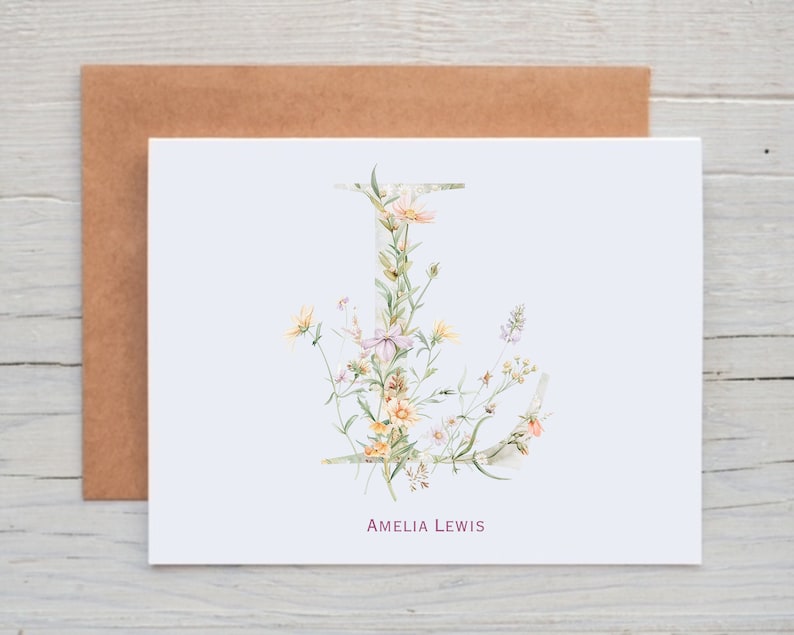 Pu&ograve; includere: Un biglietto bianco con un'illustrazione ad acquerello di una lettera J floreale. La lettera &egrave; composta da diversi fiori e foglie in tonalit&agrave; di rosa, giallo e verde. Il testo "Amelia Lewis" &egrave; stampato in rosa nella parte inferiore del biglietto.