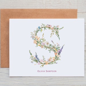 Pu&ograve; includere: Un biglietto bianco con un'illustrazione ad acquerello della lettera "S" realizzata con fiori. I fiori sono in tonalit&agrave; di rosa, giallo, blu e verde. Il nome "Olivia Sampson" &egrave; stampato in rosa nella parte inferiore del biglietto.