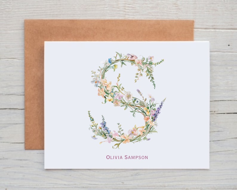 Pu&ograve; includere: Un biglietto bianco con un'illustrazione ad acquerello della lettera "S" realizzata con fiori. I fiori sono in tonalit&agrave; di rosa, giallo, blu e verde. Il nome "Olivia Sampson" &egrave; stampato in rosa nella parte inferiore del biglietto.