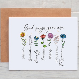May include: A white card with the text "God says you are" in black lettering. Below the text are seven colorful flowers with words underneath each flower: unique, special, lovely, precious, strong, chosen, forgiven.
