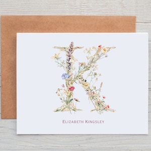 Pu&ograve; includere: Un biglietto bianco con una lettera K floreale realizzata con fiori ad acquerello. Il nome "Elizabeth Kingsley" &egrave; stampato in rosa sotto la lettera.