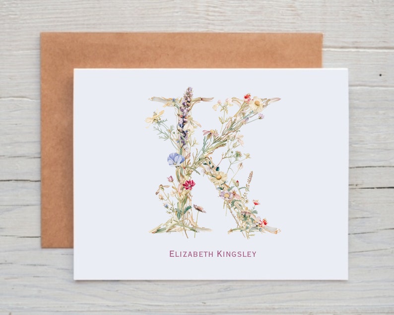 Pu&ograve; includere: Un biglietto bianco con una lettera K floreale realizzata con fiori ad acquerello. Il nome "Elizabeth Kingsley" &egrave; stampato in rosa sotto la lettera.