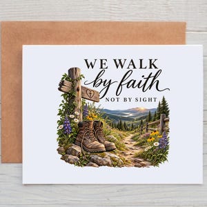 May include: A white greeting card with a brown envelope featuring a graphic of brown hiking boots, a wooden cross with a heart and cross symbol, and a mountain landscape. The text reads WE WALK by faith NOT BY SIGHT in black lettering.