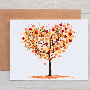 May include: A white card with a brown envelope behind it. The card features a watercolor painting of a tree with orange, red, and yellow leaves in the shape of a heart.