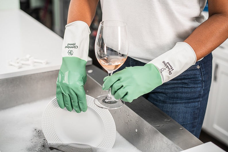 May include: A person wearing green and white dishwashing gloves is washing a white plate and holding a glass of pink wine. The gloves have the text "Cleaning Hand" printed on them.