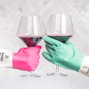 May include: Two hands wearing cleaning gloves, one pink and one green, are holding up glasses of red wine. The gloves have the text "Cleaning Hand" and "Drinking Hand" printed on them.