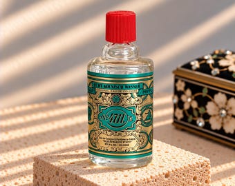 Puede incluir: Una botella de vidrio transparente de agua de colonia 4711 Echt Kölnisch Wasser con un tapón de rosca rojo brillante. La etiqueta presenta detalles ornamentados en color verde azulado y dorado con el texto 4711, Echt Kölnisch Wasser y Glockengasse N°4711 Köln a. Rh.