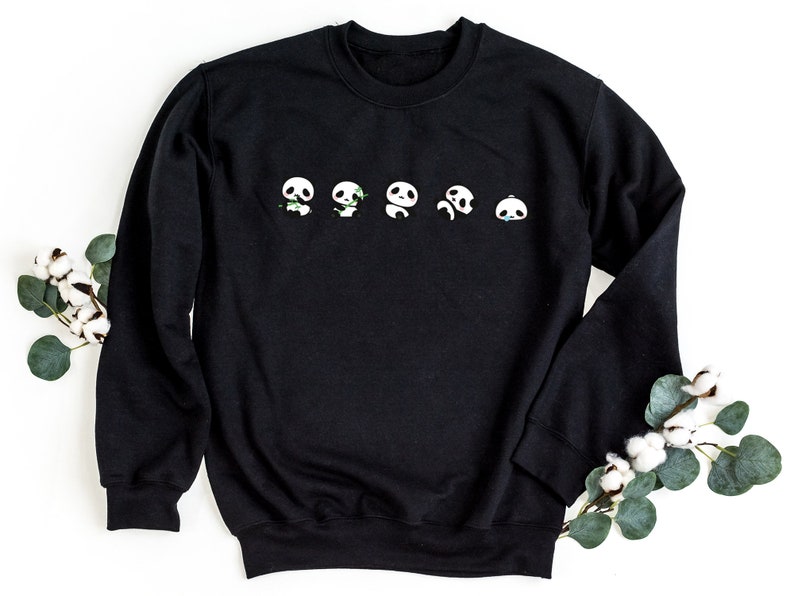 K&ouml;nnte beinhalten: Schwarzes Sweatshirt mit einer Reihe von f&uuml;nf Pandagesichtern, die auf der Vorderseite aufgedruckt sind. Jedes Panda hat einen anderen Ausdruck, darunter gl&uuml;cklich, traurig und &uuml;berrascht.